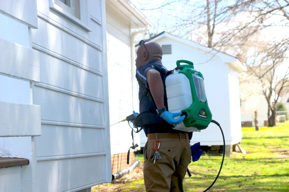 Person using a backpack sprayer outside a house