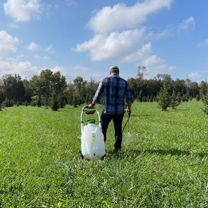 man standing in field spraying the grass with a 9-gallon sprayer