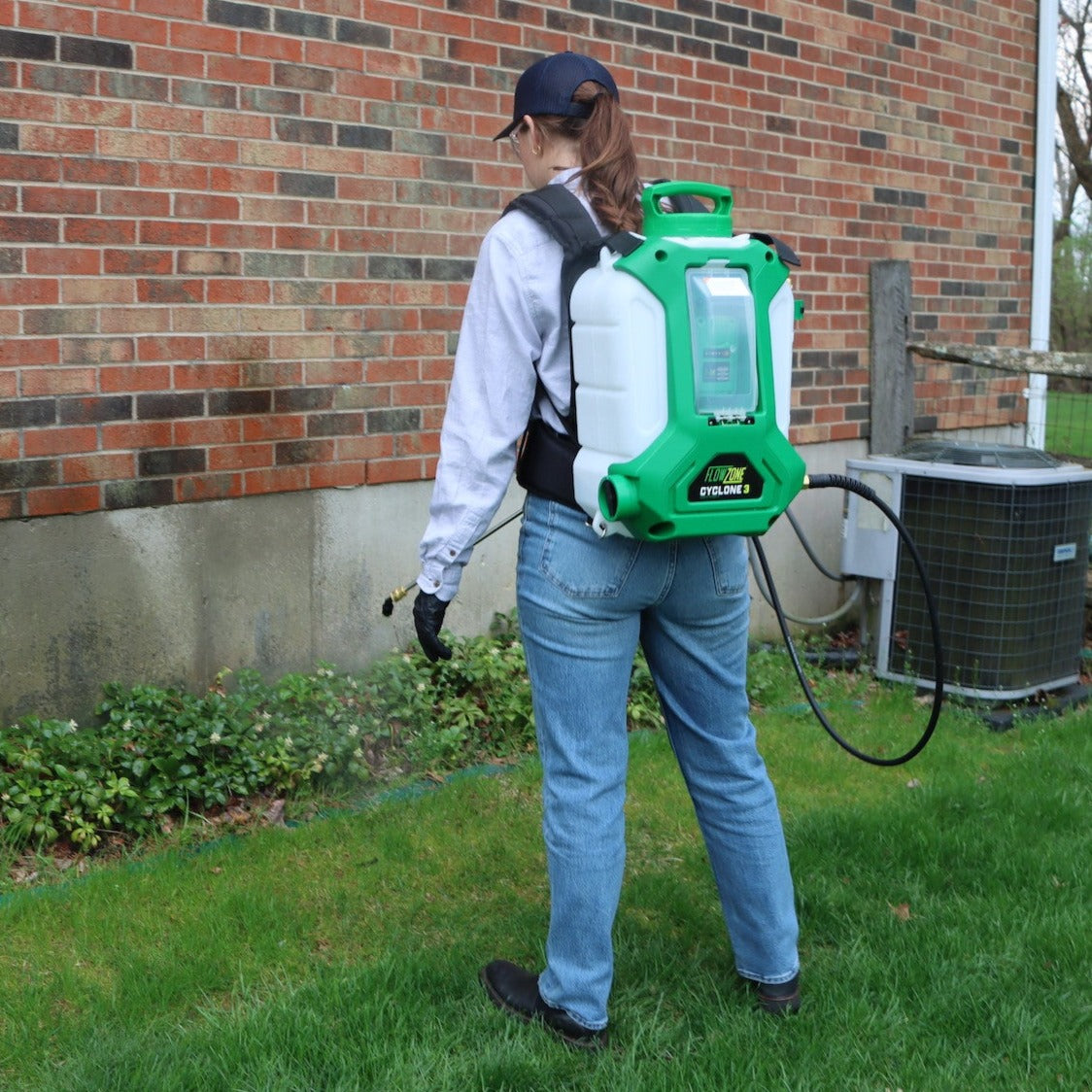 woman spraying perimeter of house with flowzone backpack sprayer